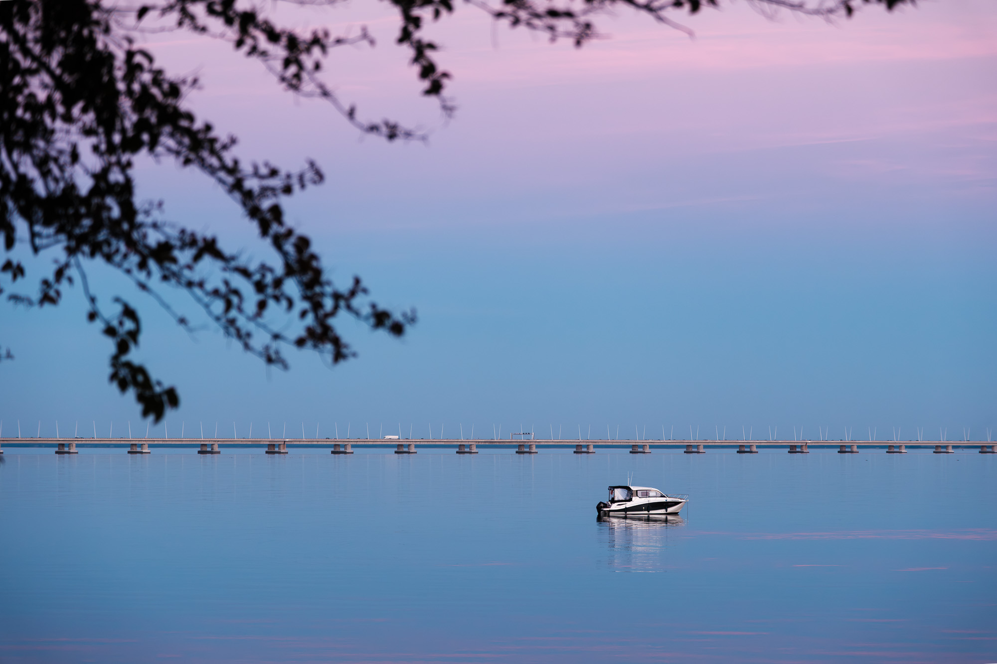 Minimalist fine art photography of the Vasco da Gama Bridge in Lisbon at twilight with a small boat on a purple-toned river.