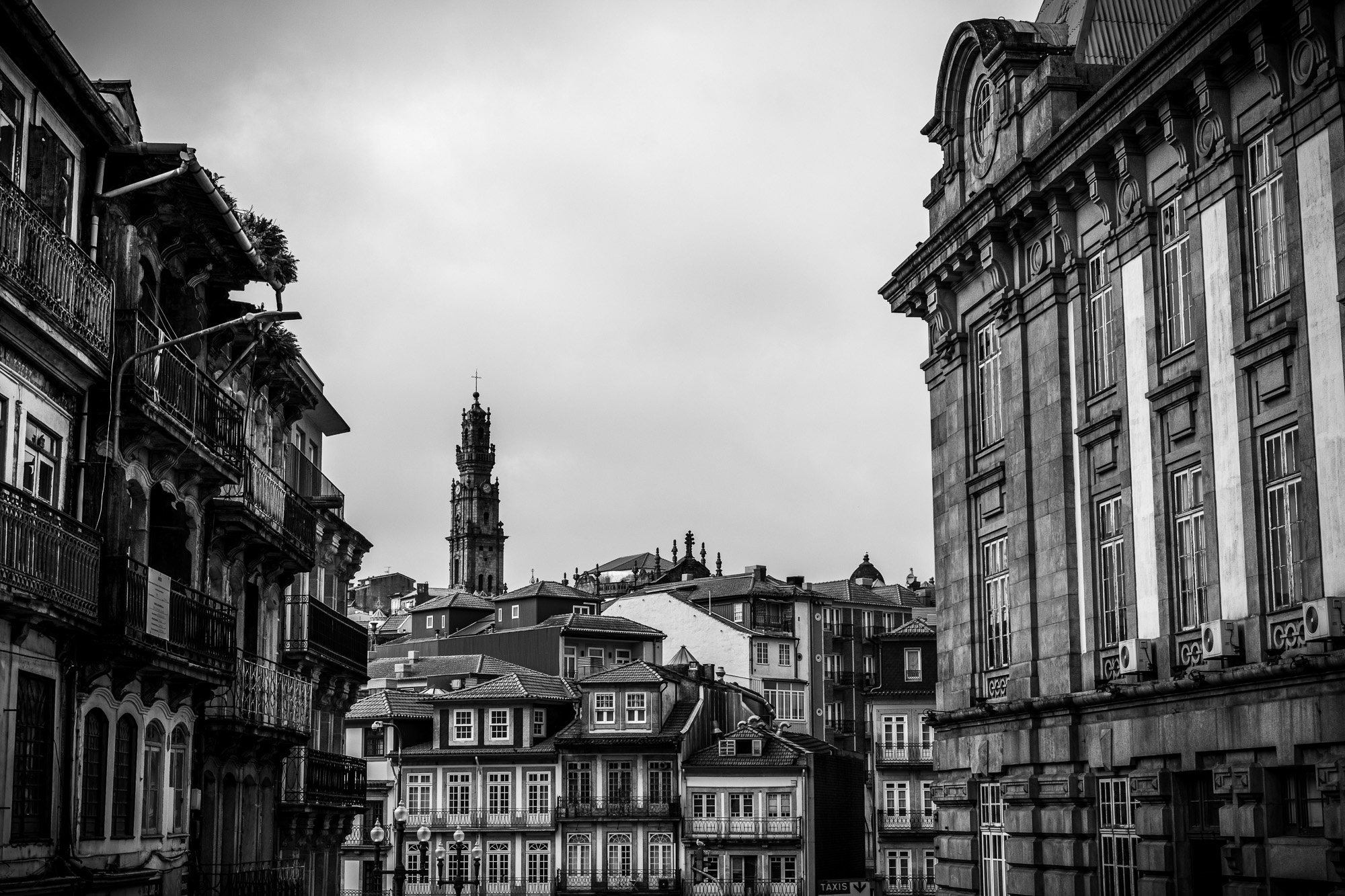 Black and white architectural photography of Porto's historic street leading to Clérigos Tower. High contrast monochrome print of Portuguese stone facades and urban perspective.